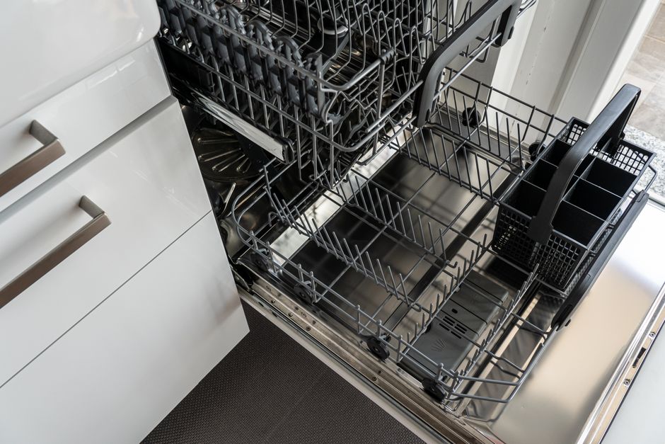 Imagem de uma cozinha moderna com a gaveta de lava-louças aberta mostrando seus compartimentos internos vazios.
