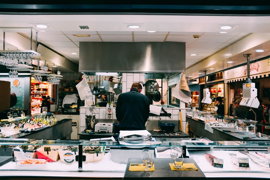 Funcionário preparando pratos em uma cozinha de restaurante movimentada, destacando a rotina de gastronomia e gestão de alimentação.