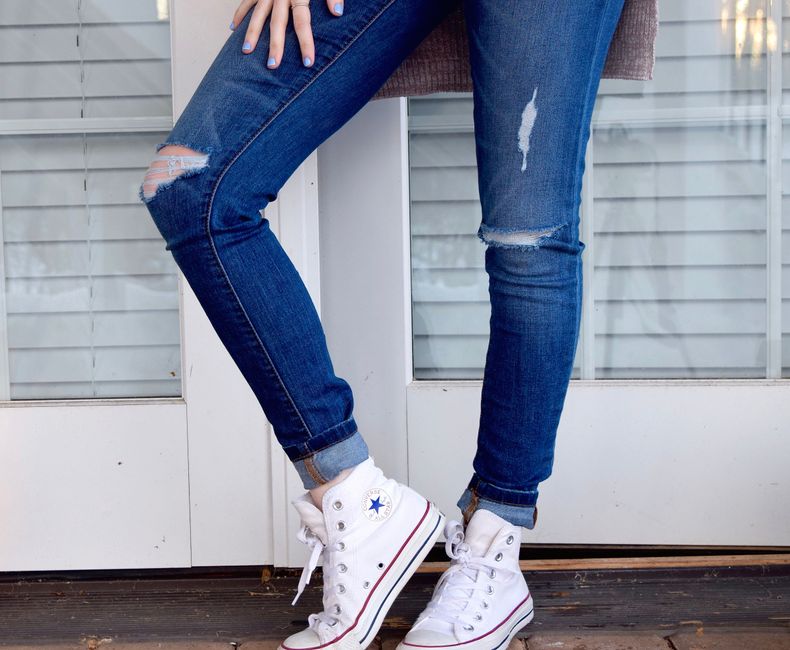 Reflexão sobre moda casual e expressão de estilo pessoal com jeans rasgados e tênis branco em ambiente urbano.