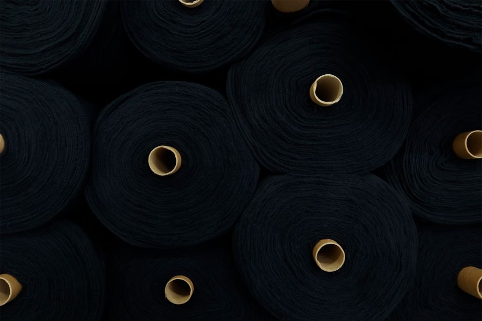 Imagem de rolos de tecido preto empilhados, sugerindo produção ou moda.