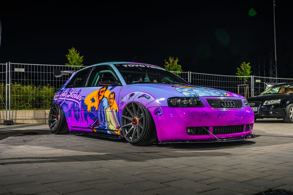 Carro esportivo com decoração vibrante e personalizada, exibido em iluminação noturna em um evento de autos tunados.