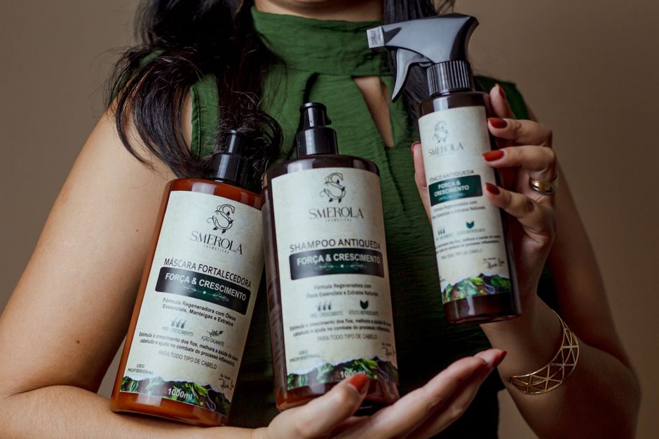 Imagem de uma pessoa segurando três frascos de produtos capilares da linha Smrela, destacando cuidados pessoais e beleza.