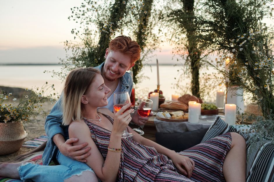 Casal celebrando um momento especial ao ar livre ao entardecer, com uma mesa de árvore decorada com velas e alimentos, em um ambiente aconchegante e romântico.