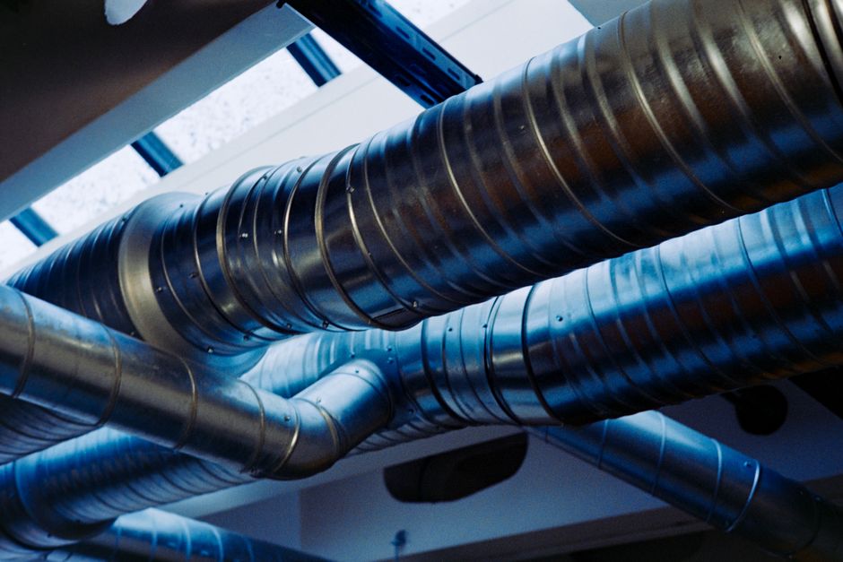 Imagem que mostra um sistema de dutos metálicos em um ambiente industrial, evidenciando infraestrutura de ventilação ou transporte de ar.