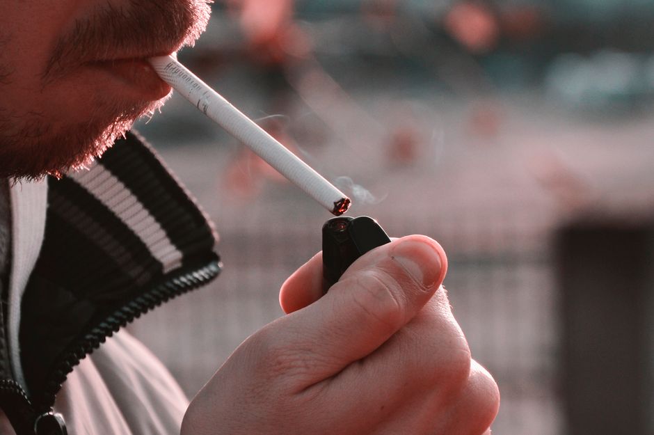 Pessoa acendendo um cigarro com um isqueiro ao ar livre, exibindo o ato de fumar.