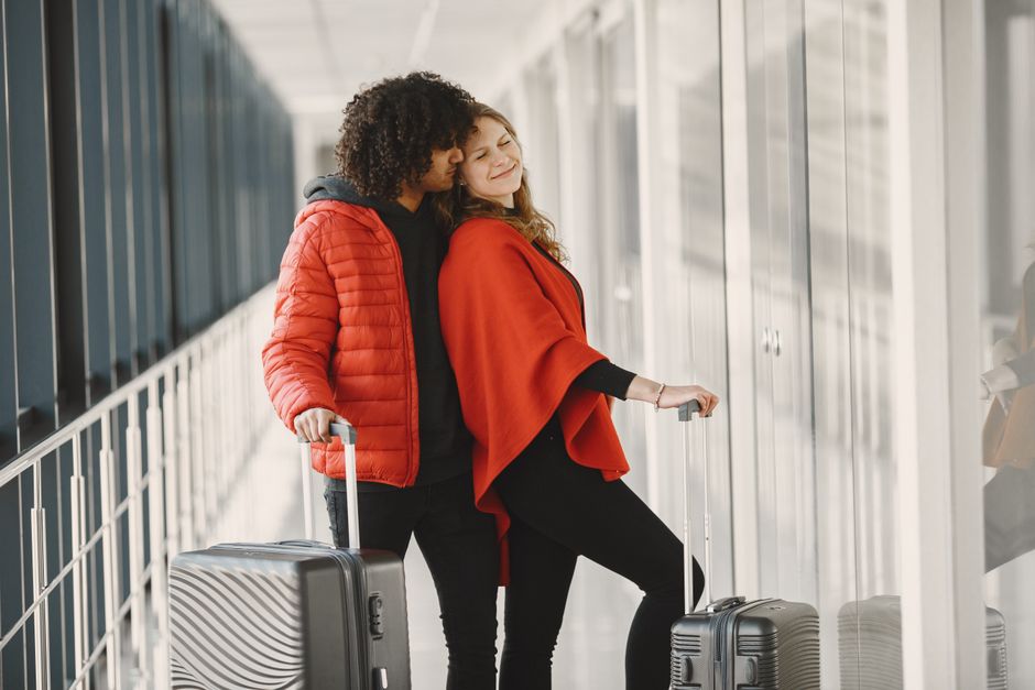 Dois viajantes felizes aguardando em um portão de embarque, prontos para viajar de férias ou lazer.