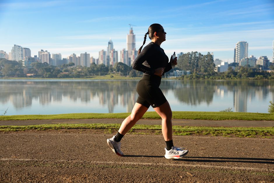 Mulher praticando running ao ar livre com cidade ao fundo, simbolizando saúde e bem-estar.