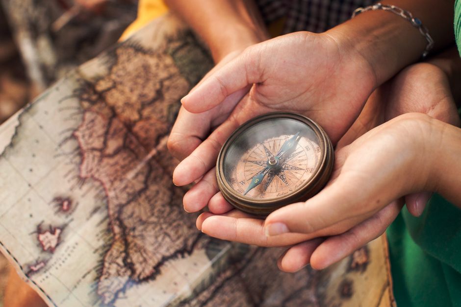 imagem de duas pessoas segurando uma bússola sobre um mapa antigo, simbolizando orientação e exploração.
