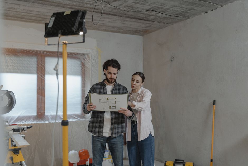 Dupla de arquitetos analisando um projeto de construção dentro de um ambiente em construção ou reforma.
