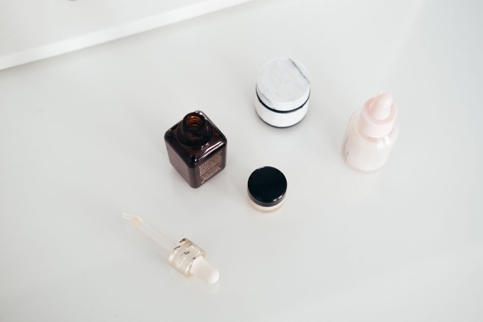 Imagem de frascos e potes de medicamentos e cosméticos sobre uma superfície branca, relacionada à saúde e cuidados pessoais.
