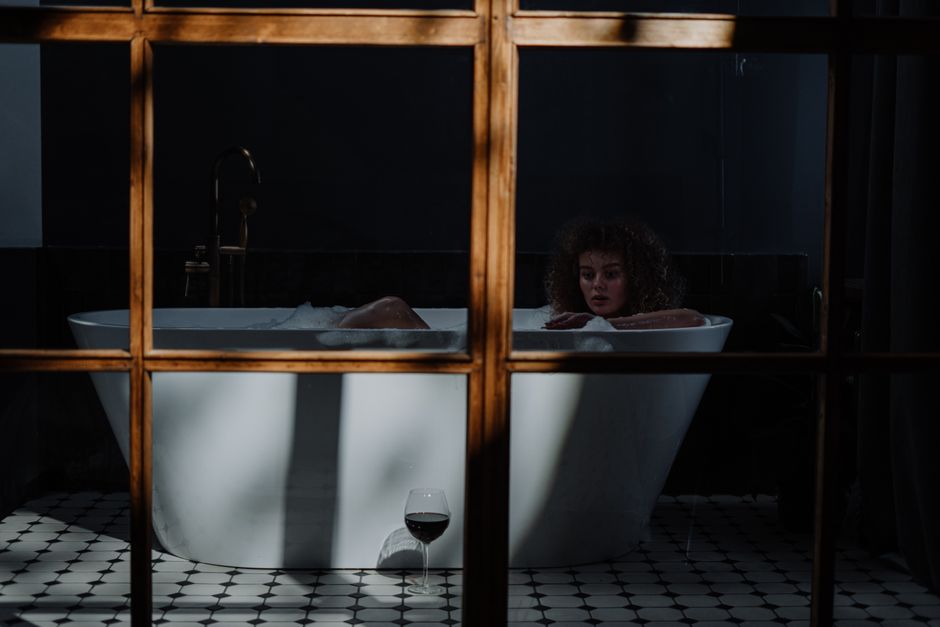 Mulher relaxando em um banho de banheira com uma taça de vinho ao lado, criando uma atmosfera de tranquilidade e autocuidado em um ambiente acolhedor e íntimo.