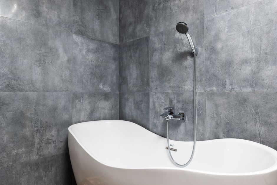Imagem de uma banheira moderna instalada em um banheiro com paredes de revestimento cinza, destacando design minimalista e elementos de conforto.
