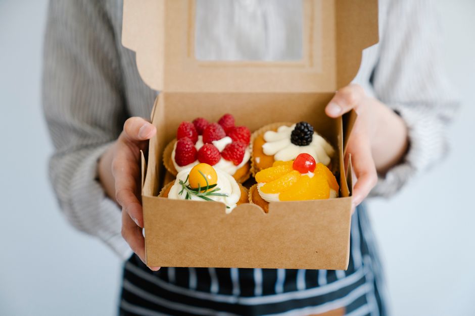 Pessoa segurando uma caixa com cupcakes decorados com frutas, ideal para ilustrar um artigo sobre doces artesanais ou festas.