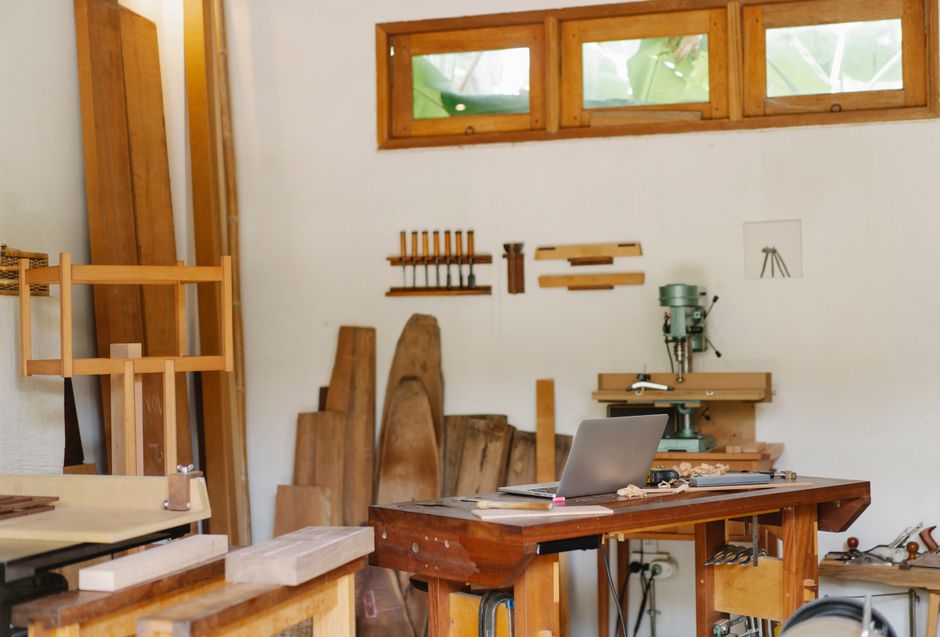 Espaço de oficina de marcenaria com ferramentas, madeira e um computador, ideal para projetos de design e produção artesanal.