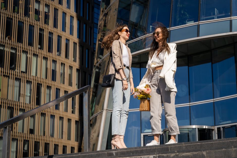 Duas mulheres conversando ao ar livre na frente de um edifício moderno, simbolizando networking ou momentos de socialização empresarial.