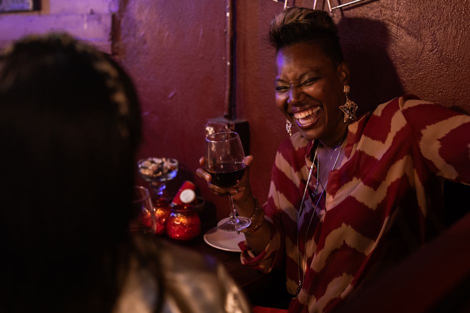 Mulher sorridente apreciando uma taça de vinho em um ambiente acolhedor, transmitindo alegria e socialização.