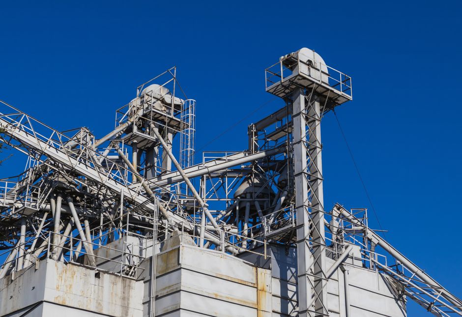 Imagem de uma estrutura industrial com torres e canais metálicos sob um céu claro, representando o setor de energia ou manufatura.
