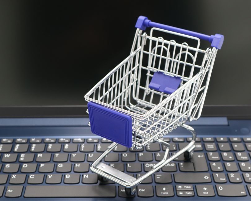 Carrinho de supermercado em miniatura colocado sobre um teclado de computador, simbolizando compras online ou comércio eletrônico.