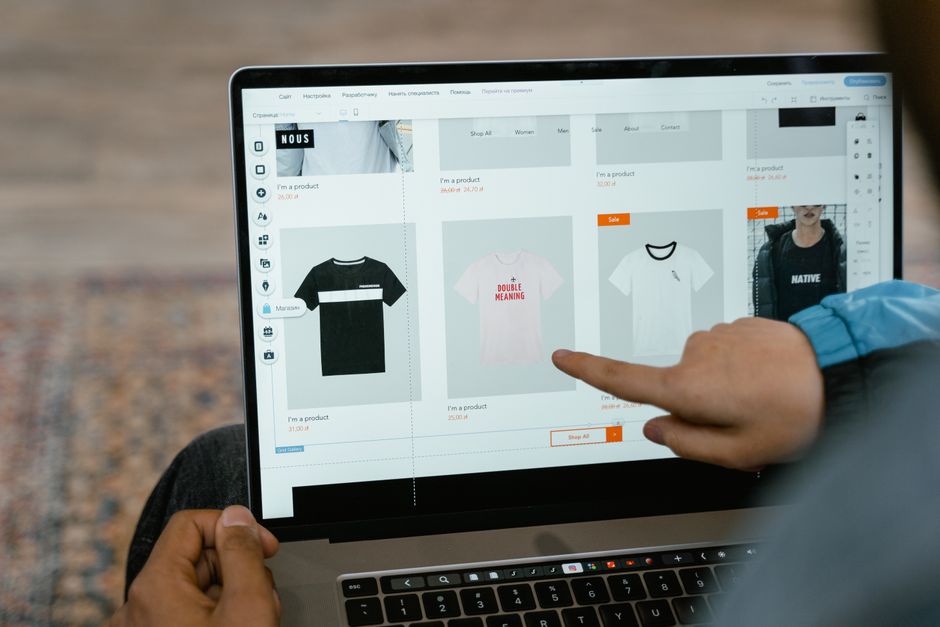 Pessoa utilizando um laptop para gerenciar produtos de moda em uma plataforma de comércio eletrônico, em ambiente externo.