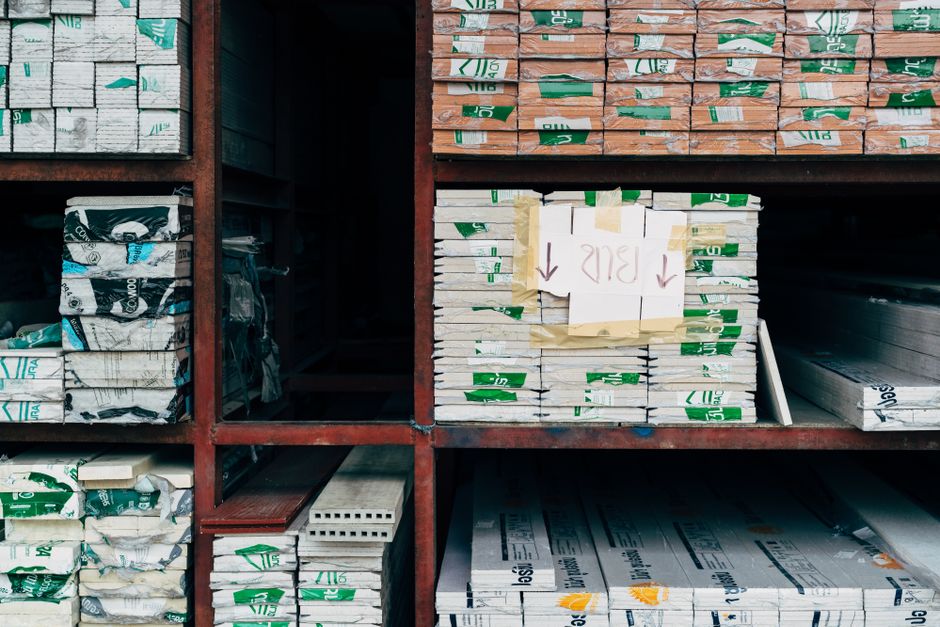 Imagem de uma estante com pilhas organizadas de materiais de construção ou papelaria, destacando o armazenamento e organização de materiais de escritório ou de obras.