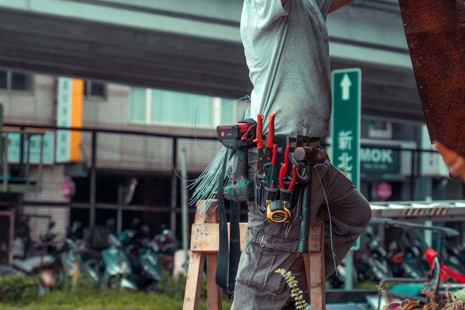 Profissional de construção civil em atividade urbana, equipado com ferramentas e segurança adequada, na execução de obras ou manutenção.