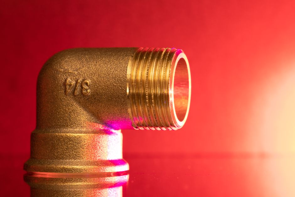 Imagem de uma conexão de tubo de metal com rosca, simbolizando engenharia ou sistemas de encanamento em um ambiente com iluminação quente.