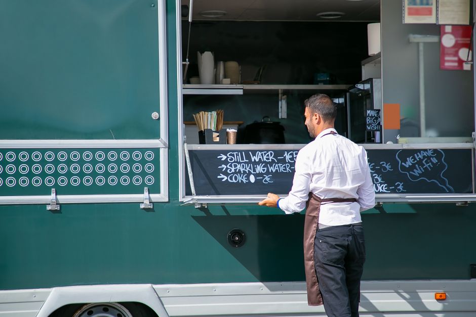 Homem trabalhando em food truck, preparando pedidos e atendendo clientes ao ar livre.
