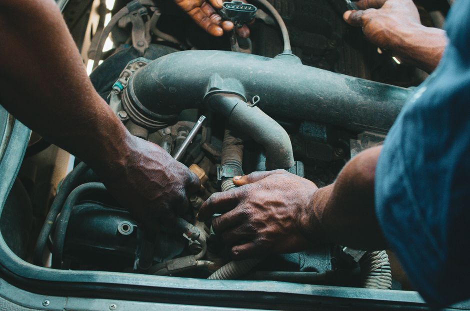 Homens realizando manutenção em um motor de veículo, indicando trabalho técnico e reparo automotivo.