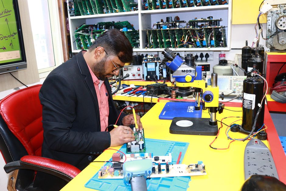 Homem em um laboratório de engenharia eletrônica trabalhando em um circuito com ferramentas e equipamentos de teste ao redor.