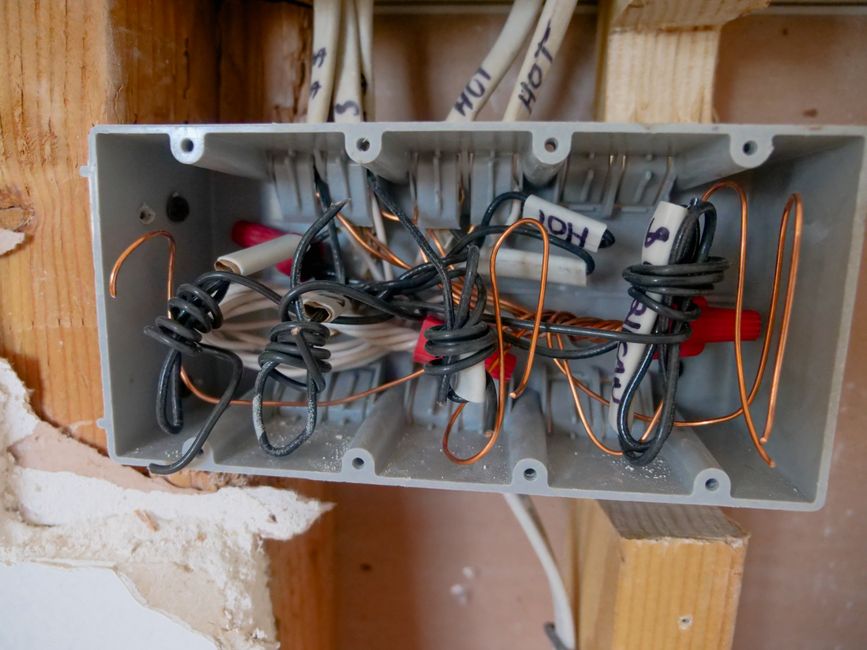 Imagem de uma caixa de distribuição elétrica com vários cabos e fios enrolados, em ambiente em construção ou reforma.