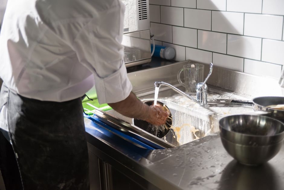 Pessoa lavando pratos na cozinha, destacando tarefas domésticas e rotina do dia a dia.