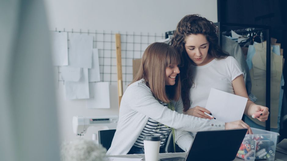 Duas mulheres colaborando em um ambiente de trabalho criativo e inovador, analisando ideias e estratégias juntas.