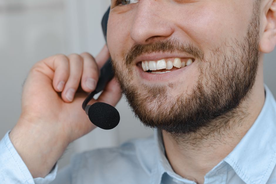 Homem sorridente atendendo ao cliente ao telefone, representando atendimento ao cliente ou suporte técnico em ambiente de escritório.