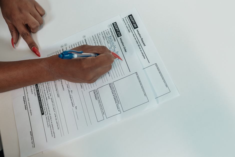 Pessoa preenchendo um formulário de adoção, representando ações burocráticas e processos administrativos.