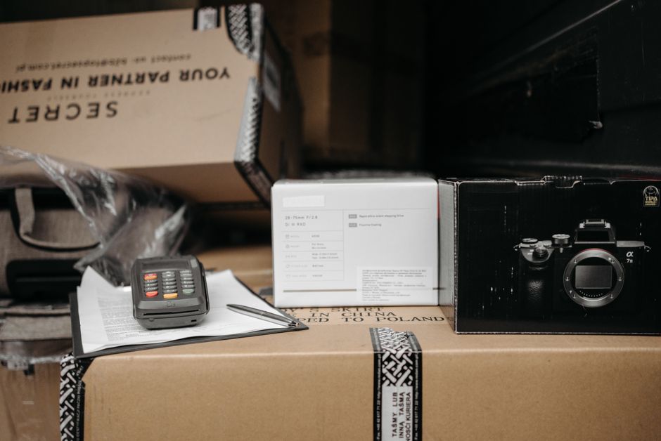Imagem de uma área de armazenamento ou inventário com caixas, câmera e itens de documentação, sugerindo organização de equipamentos ou produtos.