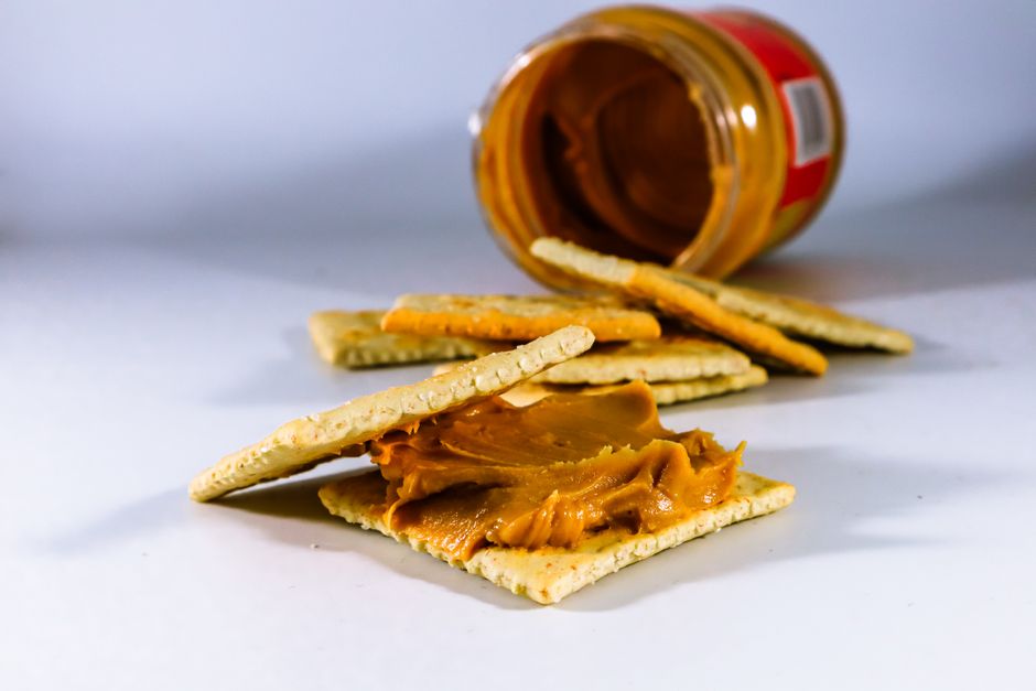 Imagem de bolachas recheadas com pasta de amendoim, com um pote de pasta ao fundo, representando alimentos e nutrição.