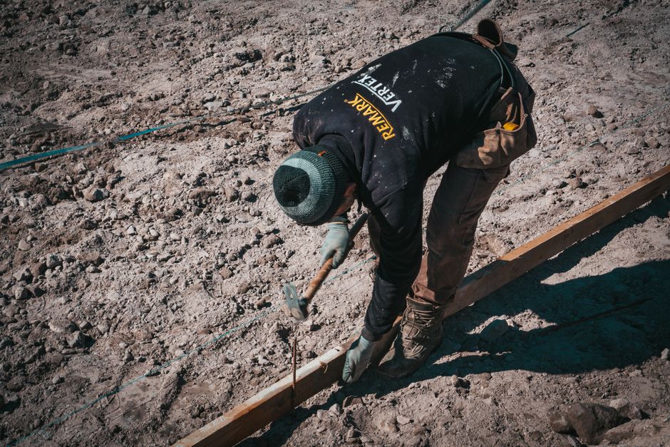 Imagem de um trabalhador em obra civíl, utilizando ferramentas para nivelar o solo na construção.