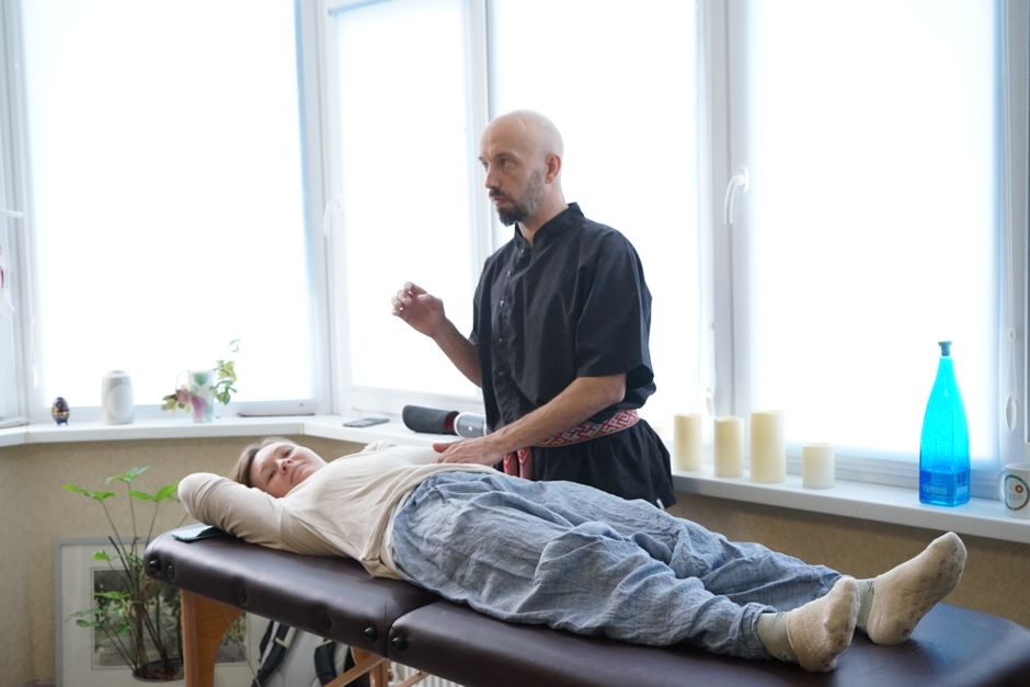 imagem de uma sessão de terapia ou prática de cura holística, com um praticante ao lado de um paciente deitado em uma maca, em ambiente iluminado e tranquilo