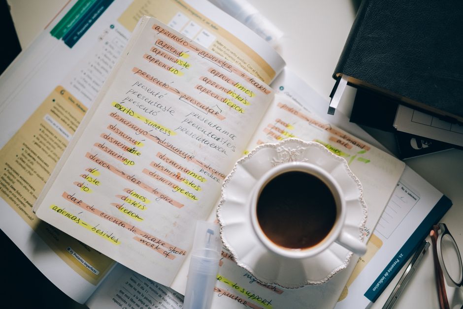 Estudo e revisão de vocabulário em um ambiente de trabalho, com materiais de leitura, destaques e um café ao lado.