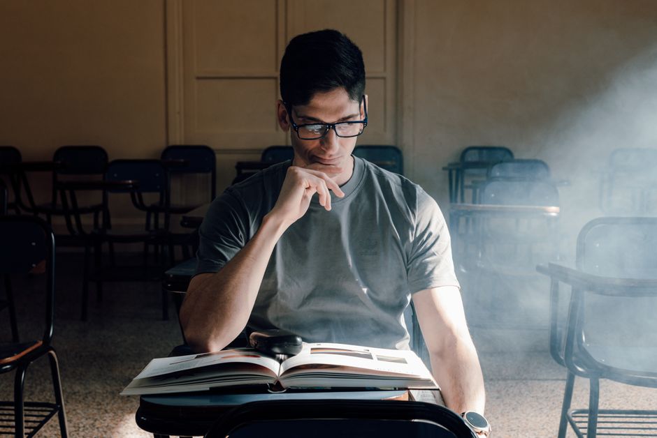 Estudante concentrado estudando sozinho em uma sala de aula vazia, refletindo sobre o conteúdo acadêmico.