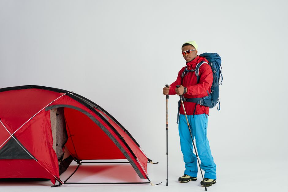 Imagem de um montanhista com roupas de aventura, mochila e bastões, ao lado de uma barraca de camping, pronto para explorar a natureza.