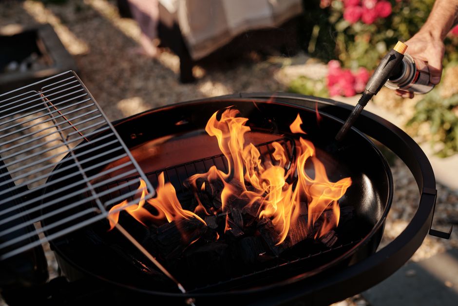 Imagem de um churrasco ao ar livre com fogo controlado sendo preparado com um queimador a gás.