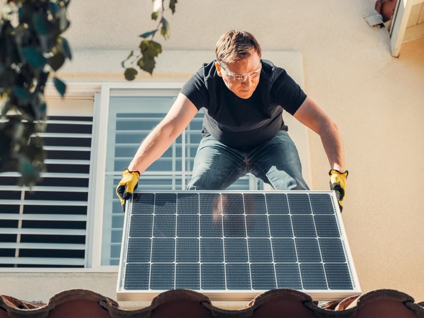 Homem instalando painéis solares para energia sustentável em sua residência.