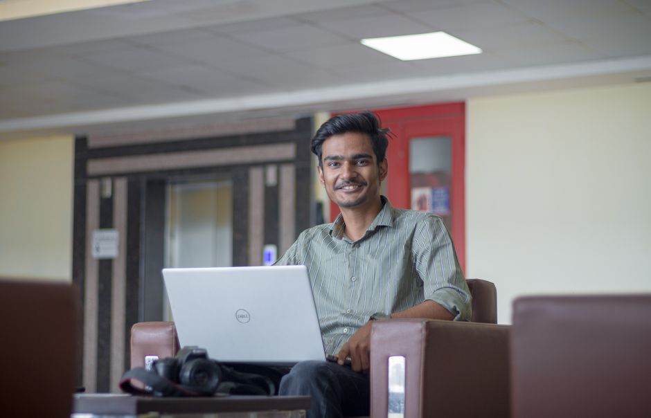 Jovem profissional sorridente usando laptop em ambiente de coworking, transmitindo produtividade e tecnologia.