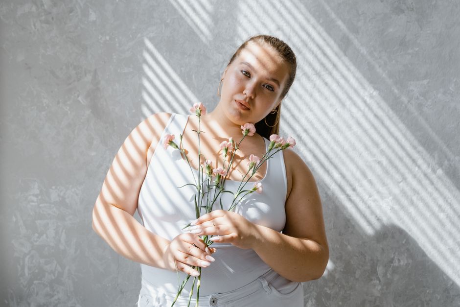 Mulher segurando flores em um ambiente com iluminação natural, transmitindo serenidade e conexão com a natureza.