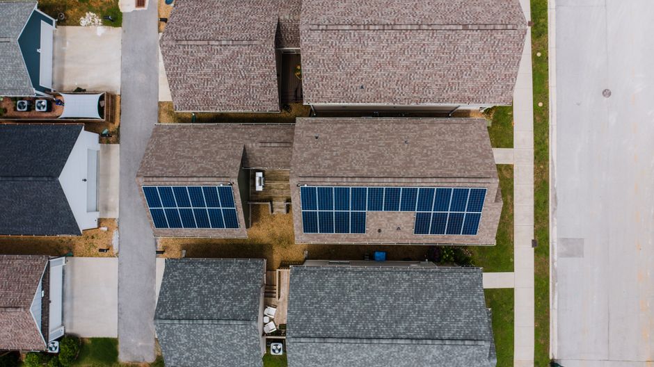 Visão aérea de casas residenciais com painéis solares instalados nos telhados, destacando a adoção de energia sustentável em ambientes domésticos.