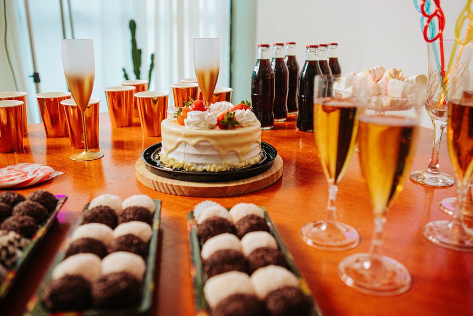Celebração de aniversário com bolo, drinks e docinhos em um ambiente festivo.
