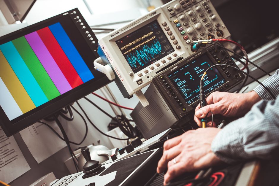 Imagem de um profissional realizando testes e análises técnicas usando equipamentos eletrônicos em um ambiente de trabalho tecnológico.