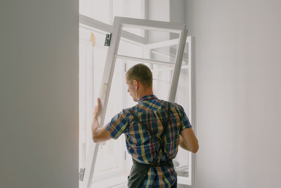 Homem instalando uma janela de vidro em uma parede de ambiente interno com iluminação natural.