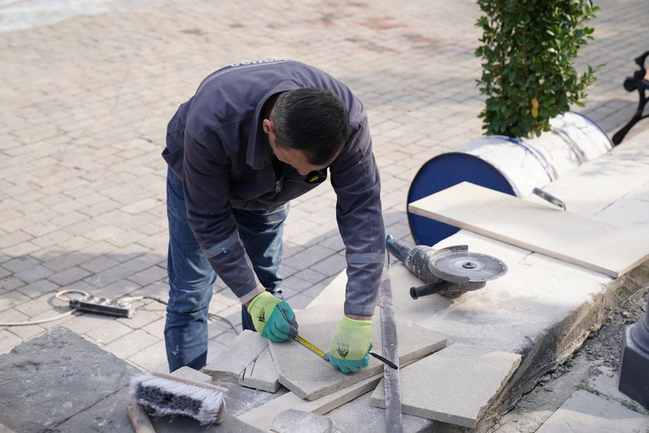 Homem realizando reformas em calçada, cortando e ajustando pedras em espaço ao ar livre.
